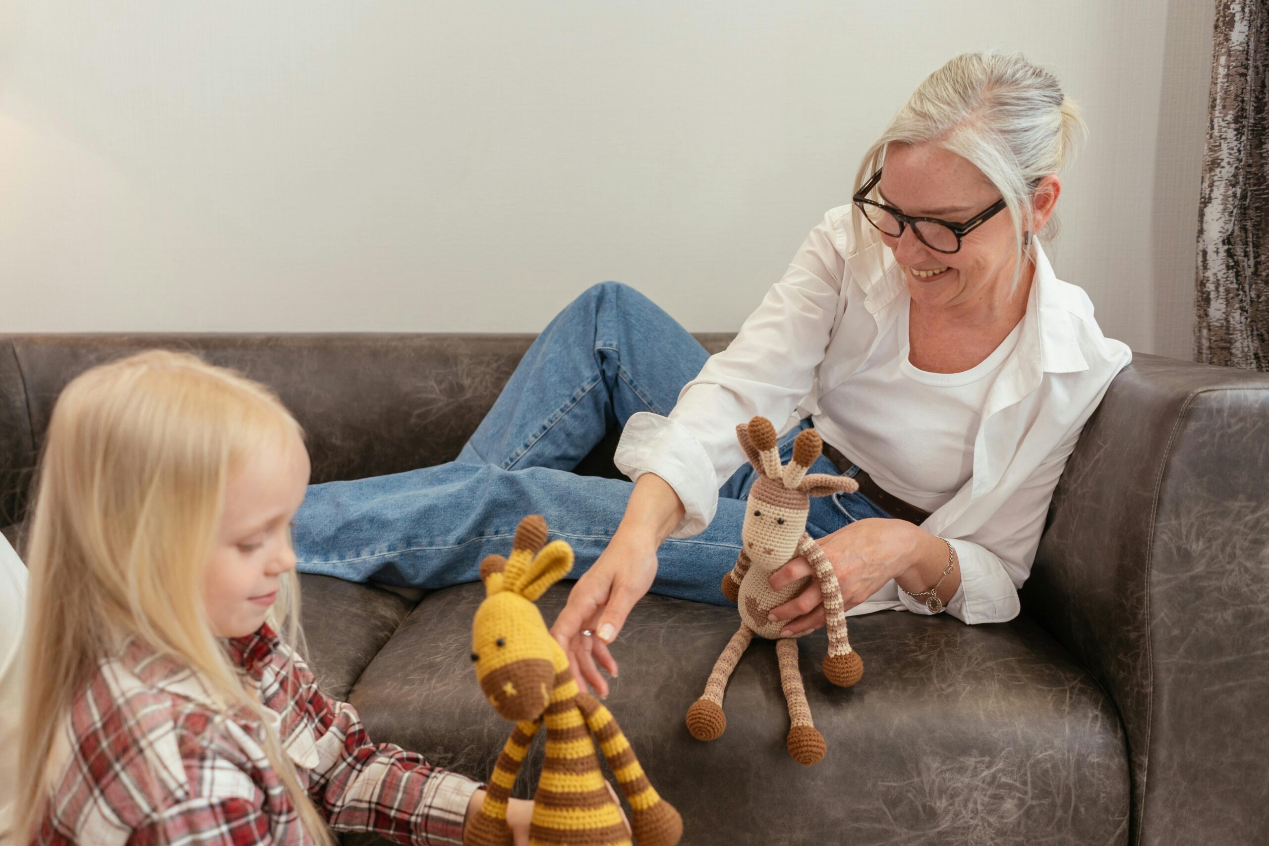 Woman and child playing with crocheted giraffe toys on a couch, emphasizing family bonding and nurturing moments.