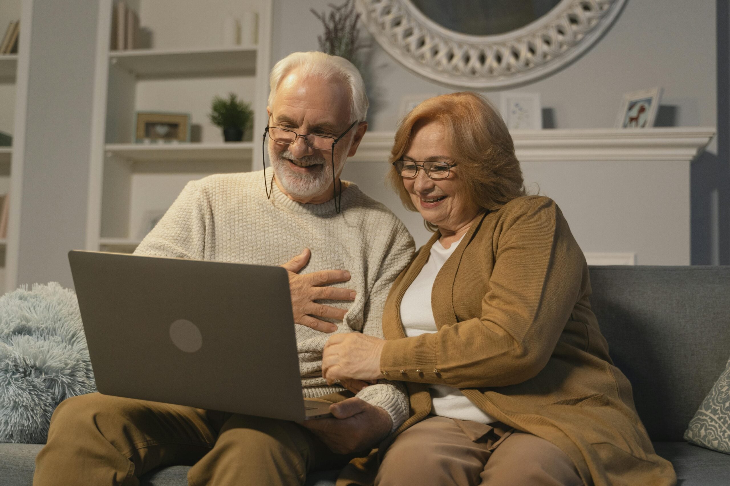 Elderly couple smiling while using a laptop together, showcasing engagement and connection, relevant to planning for end-of-life expenses in the context of funeral and burial insurance.