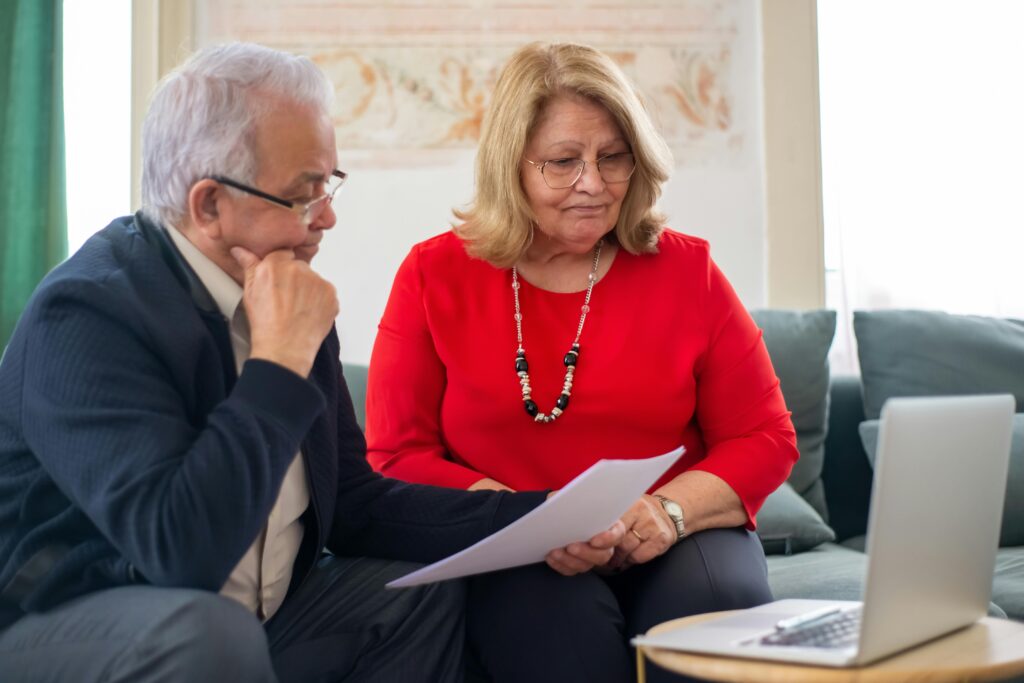 Older couple discussing plans while reviewing documents related to end-of-life arrangements, emphasizing the importance of proactive funeral planning and burial insurance options.